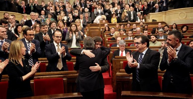 El presidente catalán en funciones, Artur Mas (de espaldas), saluda a Carles Puigdemont, poco antes de comenzar el pleno del Parlament en el que se debate la investidura de Puigdemont como nuevo presidente de la Generalitat, tras el pacto alcanzado ayer