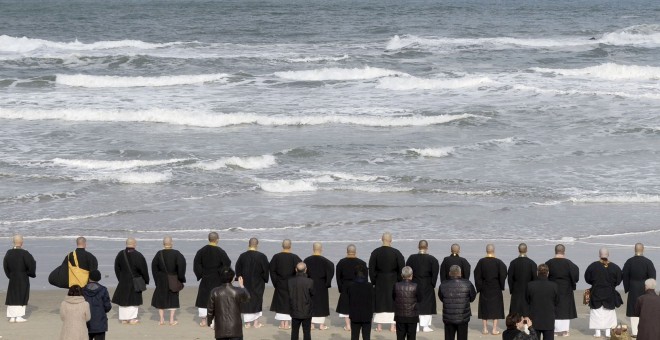 Monjes budistas y familiares de las víctimas, frente al mar, rezan en recuerdo de los fallecidos por e tsunami de marzo de 2011. REUTERS/Kyodo
