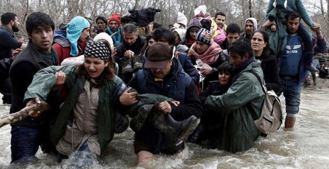 Varios refugiados  usan una cuerda para cruzar un río en la frontera entre Grecia y Macedonia. / YANNIS KOLESIDIS (EFE)