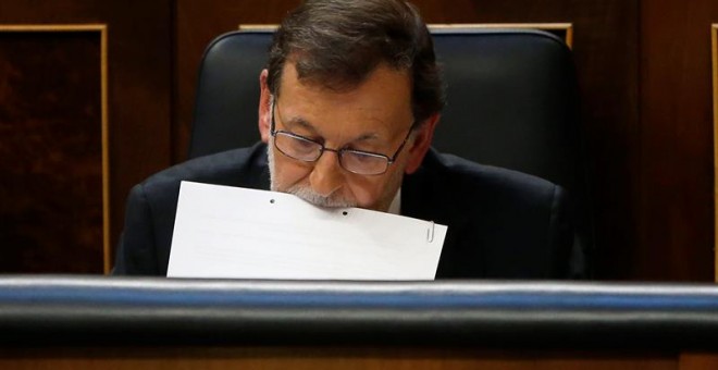 El presidente del Gobierno en funciones, Mariano Rajoy, sujeta unos papeles con la boca durante el pleno del Congreso de los Diputados donde ha comparecido hoy de forma extraordinaria y por vez primera en esta legislatura para informar de los resultados d