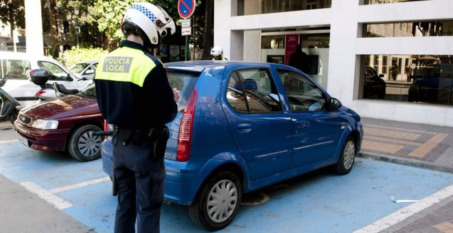 Un Policía Local impone una multa a un vehículo por estacionar en una plaza de minusválido.