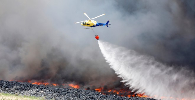 Un helicóptero trata de sofocar las llamas del incendio de neumáticos en Seseña.- REUTERS/Sergio Perez