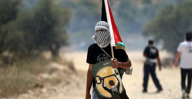 Un manifestante enmascarado sostiene una bandera palestina durante los enfrentamientos con soldados israelíes en una protesta delante del día de la Nakba , en la localidad cisjordana de Bilin cerca de Ramallah, 13 de mayo de 2016. REUTERS / Mohamad Torokm