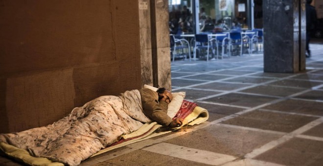 Un hombre sin techo duerme en la acera, junto a una cafetería. EFE