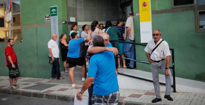 Dos hombres se abrazan mientras la gente espera para entrar a una oficina de empleo en el centro de Málaga. REUTERS/Jon Nazca