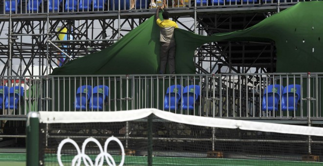 Operarios colocando carteles tirados por el viento en el centro olímpico de tenis. /REUTERS