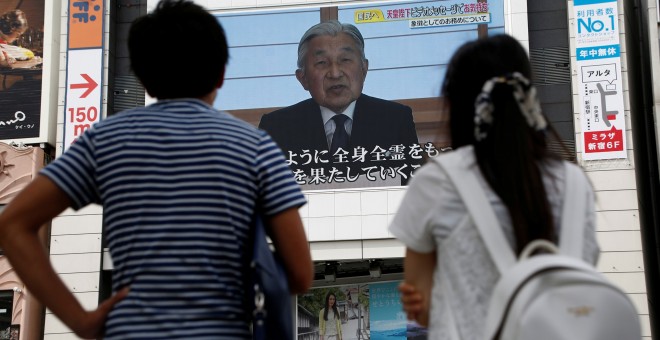 Un par de personas observan en una pantalla en la calle en Tokio el mensaje del emperador Akijito. REUTERS/Kim Kyung-Hoon