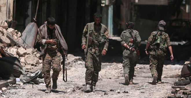 Combatientes de las Fuerzas Democráticas de Siria (SDF) caminan sobre los escombros de tiendas y edificios dañados en la ciudad de Manbij, en Alepo, Siria. REUTERS / Rodi Said