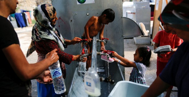 Anis, de cuatro años, lava su ropa en una fuente del campo de refugiados de Chios, en Grecia, junto a su madre/REUTERS