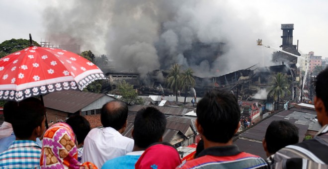 Varias personas miran las labores de extinción del incendio en Daca. REUTERS/Mohammad Ponir Hossain