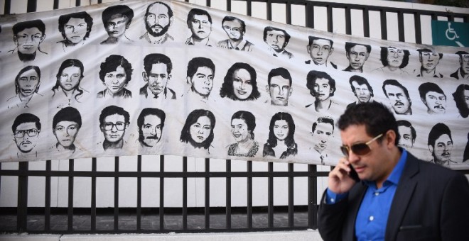 Un hombre pasa en Ciudad de Guatemala junto a un mural con rostros de desaparecidos durante el conflicto armado. - AFP