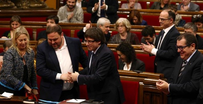 El presidente de la Generalitat, Carles Puigdemont (c), felicita al vicepresidente y conseller de Economía, Oriol Junqueras (i) el pasado día 20 en el Parlament. /EFE