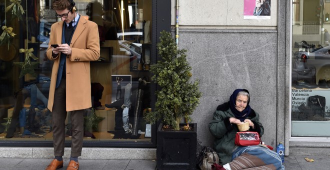 Un hombre consulta a su móvil junto a una tienda en cuya puerta hay una mujer pidiendo limosna, en el madrileño barrio de Salamanca. AFP/Gerard Julien