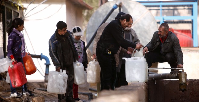 Habitantes de Damasco llenan bidones de agua en un suburbio controlado por el régimen de Al Asad. - REUTERS