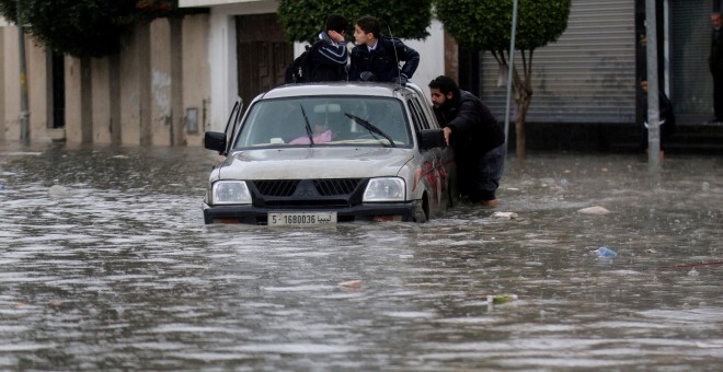 La gente empuja un vehículo a través de una calle inundada después de la lluvia en Trípoli/REUTERS
