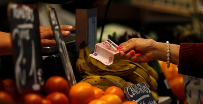 Una mujer paga después de hacer la compra en un puesto de frutas y verduras en un mercado en Málaga. REUTERS/Jon Nazca