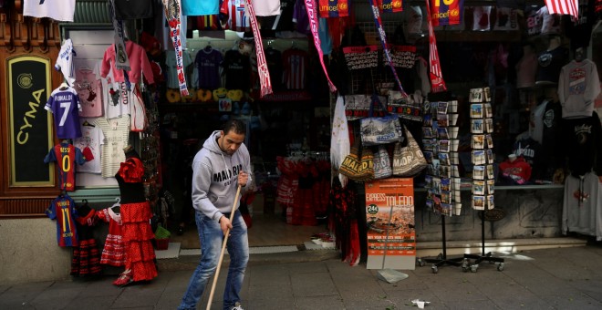 El empleado de una tienda de objetos turísticos del centro de Madrid barre la acera. REUTERS/Susana Vera