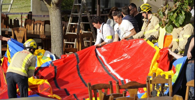 Varios operarios y bomberos retiran el castillo hinchable del restaurante Mas Oller, de Caldes de Malavella (Gerona), que ha volado unos 40 metros por encima del tejado del establecimiento, provocando la muerte de una niña, y causando heridas muy graves a