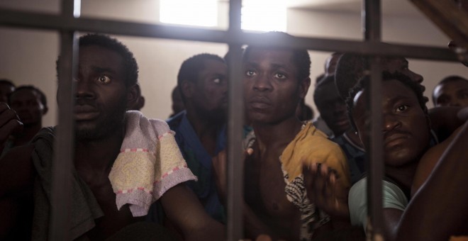 Ocho migrantes subsaharianos suplican su liberación en el centro de detención de Surman. El director del centro (no fotografiado) está de pie frente a la celda, amenazando golpearlos con un bastón si no se calman. Los detenidos se permanecen inmóviles del