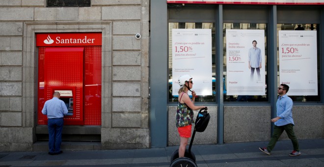 Un hombre utiliza un cajero automático del Banco Santander junto a una oficina del Popular, en Madrid. /Juan Medina