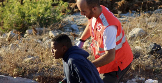 Un efectivo de la Cruz Roja con uno de los inmigrantes que ha sido abandonado, junto con otros once de los cuales uno ha fallecido, por seis motos de agua que los transportaban a pocos metros de la orilla de una de las playas de la barriada de Benzú, en C