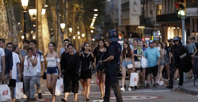 Un grupo de gente se desplaza esta noche entre el despliegue policial en el lugar del atentado ocurrido por la tarde en las Ramblas de Barcelona, un atropello masivo en el que una furgoneta ha arrollado a varios peatones que paseaban por la zona, y en el