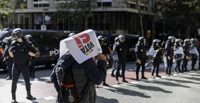 Una persona con un cartel en favor del Sí en el referéndum del 1-0 pasa delante de los antidisturbios de la Policái Nacional desplegadas ante la se sede del CUP. | XAVI HERRERO