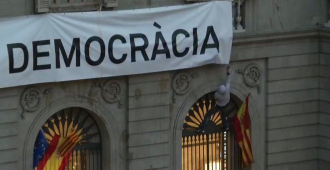 Moment en què uns encaputxats intententen despenjar la pancarta amb l'expressió 'Més democràcia' de la façana de l'Ajuntament