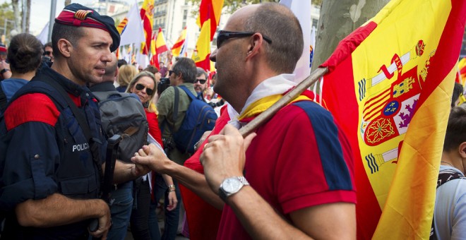 Un hombre con la bandera de España saluda a un mosso de esquadra durante la manifestación convocada por Societat Civil Catalana, Espanya i Catalans y otras entidades contrarias a la independencia con motivo del Día de la Fiesta Nacional. EFE/Andreu Dalmau