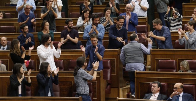 Joan Mena, de espaldas, sube a su escaño entre los aplausos de Podemos. / EFE