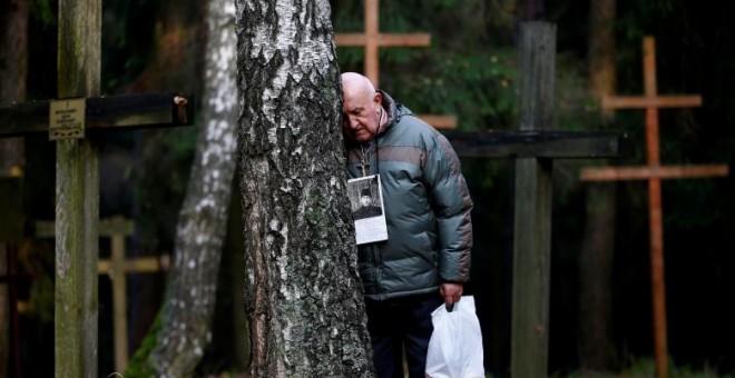 Un hombre reposa su cabeza contra un árbol en Kuropaty, donde se rinde homenaje a las víctimas del estalinismo./REUTERS