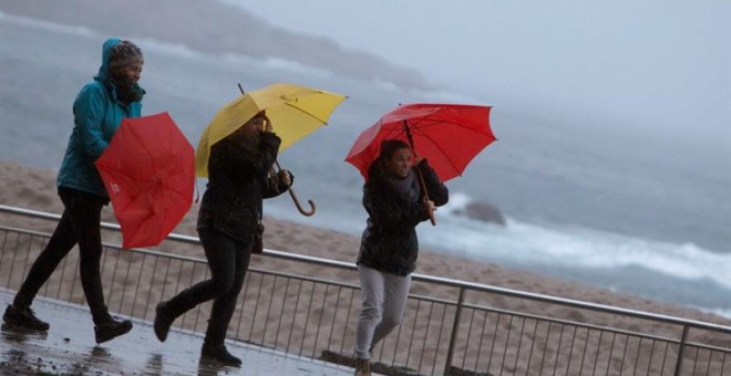 Tres mujeres se protegen de la lluvia en el paseo marítimo de A Coruña. - EFE