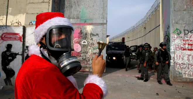 Un manifestante palestino vestido de Papá Noel protesta ante tropas israelíes en el muro que rodea la ciudad de Belén, ayer sábado 23 de diciembre. REUTERS/Ammar Awad