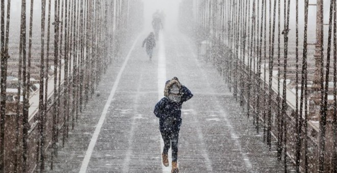 Peatones se protegen de la nieve y del viento mientras cruzan el puente de Brooklyn durante una tormenta de viento y nieve en Nueva York (Estados Unidos), hoy 4 de enero de 2017.EFE
