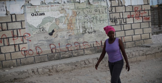 Una mujer pasa frente a un cartel de Oxfam en Corail, campamento para desplazados a las afueras de Puerto Príncipe, Haití. / Reuters