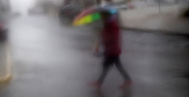 Un viandante, visto a través de un cristal, cruzando una calle en Espartinas (Sevilla), durante una intensa tromba de agua registrada esta semana en la ciudad. EFE