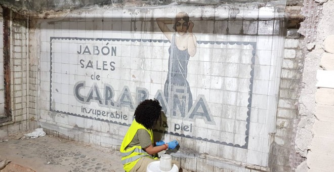 Operaria limpia los azulejos del mural publicitario datado en los años 20 y descubierto en las obras de la estación de metro Sevilla, en Madrid. / Consejería de Cultura
