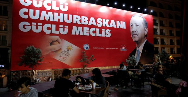 Personas en la terraza de un restaurante mientras, de fondo se puede ver un cartel preelectoral de Erdogan. - REUTERS