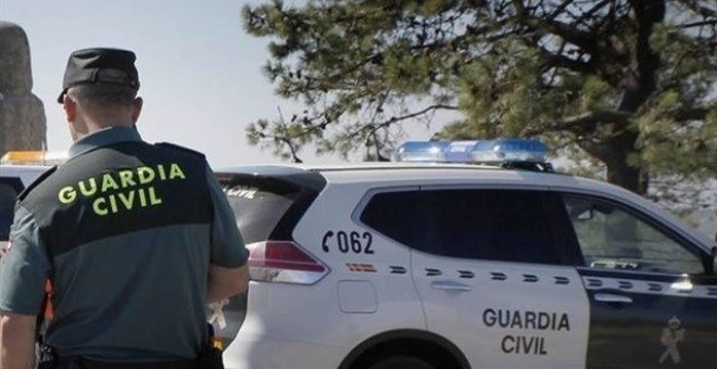 Agente de la Guardia Civil junto a un coche patrulla. GUARDIA CIVIL