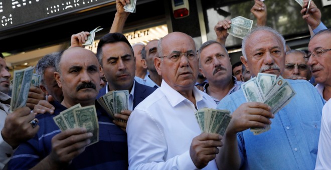 Varias personas sostiene billetes de dólar delante de una oficina de cambio em Ankara, respondiendo a la llamada del presidente Erdogan a cambiar billetes verdes par sostener la lira turca. REUTERS/Umit Bektas
