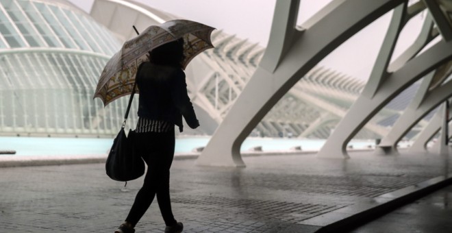 Una mujer se refugia de la lluvia con un paraguas en la Ciudad de las Ciencias de València./EFE