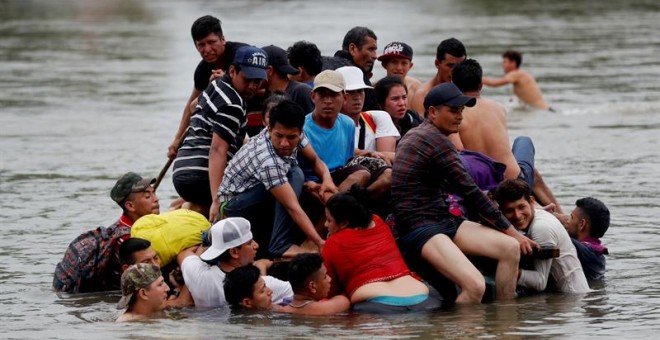 Decenas de migrantes hondureños cruzan a pie y el balsa el río Suchiate, que separa a Guatemala de México, mientras otros observan desde un puente. EFE/Esteban Biba