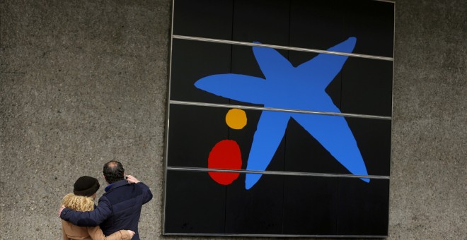 Una pareja se hace un selfi junto al logo de Caixabank en su sede en Madrid. REUTERS/Sergio Perez