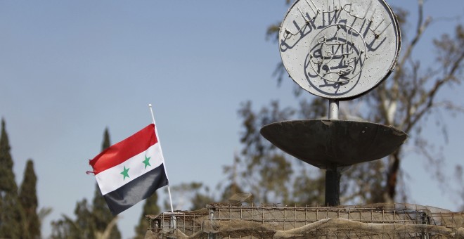 Una foto de archivo de una bandera nacional siria ondeando junto al eslogan del Estado Islámico en una rotonda donde las ejecuciones fueron llevadas a cabo por militantes de ISIS en la ciudad de Palmira./REUTERS