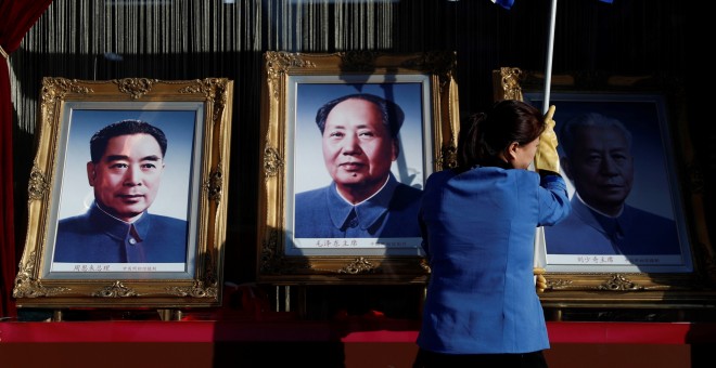Una trabajadora limpia el cristal de un escaparate donde se exponen fotografías de los exlíderes chinos Mao Tse tung (c), Zhou Enlai (i) y Liu Shaoqi (d) en la calle Wangfujing en Pekín (China). EFE/ Wu Hong