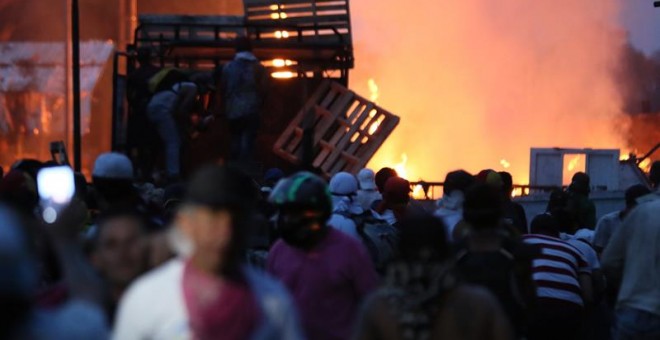 Manifestantes se enfrentan con miembros de la Policía Nacional Bolivariana, junto a un camión que transportaba ayuda humanitaria y fue quemado, este sábado, en el puente Francisco de Paula Santander, en la frontera entre Cúcuta (Colombia) y Venezuela. EFE