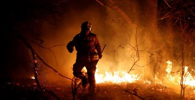 Los bomberos intentan sofocar el incendio que se ha producido hoy en los alrededores de Labares. Un total de 77 incendios se encuentran activos en Asturias, contra los que luchan unas 200 personas, a las que se sumarán mañana, lunes, otro centenar aportad