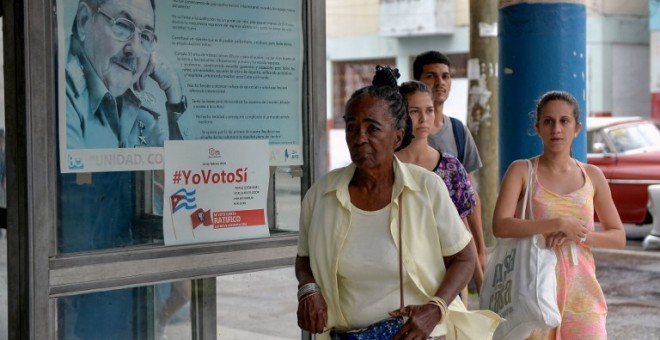 Una mujer pasa junto a un cartel del ex presidente cubano Raúl Castro y un cartel de la campaña del gobierno que lee '#Ivoteyes' en referencia a la nueva Constitución, aprobada recientemen en referéndum. APF/Yamil Lage