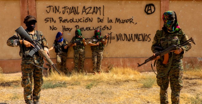 Brigadistas del IRPGF posan junto a milicianas de las YPG, junto a una pintada en castellano con lemas contra el patriarcado. | IRPGF