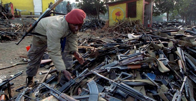 A Zairean soldiers inspects piles of weapons confiscated to Rwandan government troops after they fled the border city of Gicenyi, Rwanda July 18, 1994. REUTERS/Corinne Dufka/File Photo